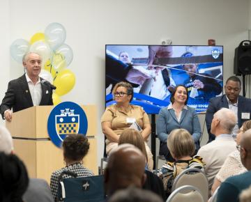 john gismondi speaks at a podium for an announcement event of the gismondi neighborhood education program