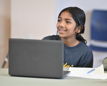 a smiling elementary school aged child sitting in front of a laptop